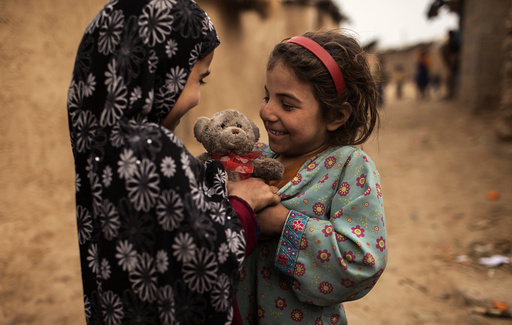 Afghan refugees smile as a girl presents a stuffed toy with a heart-shaped ribbon to her friend on Valentine's Day in a slum on the outskirts of Islamabad