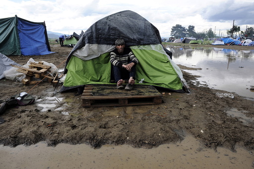 A refugee sits at the entrance of his tent following heavy rainfall at a makeshift camp for migrants and refugees at the Greek-Macedonian border near the village of Idomeni
