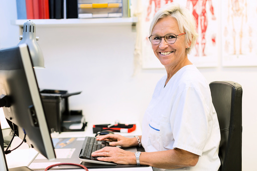 Portrait of happy senior orthopedic surgeon using computer at desk in clinic