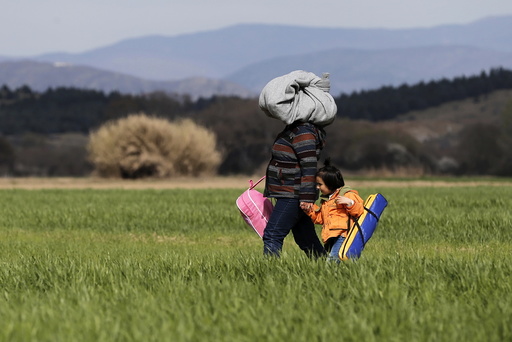 A migrant walks with a child through a field towards a makeshift camp at the Greek-Macedonian border, near the village of Idomeni