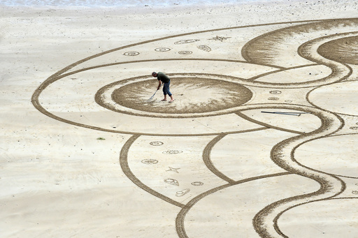 Sand artist Marc Treanor creates a work on the North Beach at Tenby Harbour, Pembrokeshire, Wales