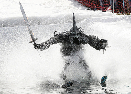 Skier in costume attempts to cross pool of water at foot of ski slope while competing in annual 