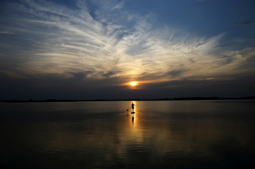 A boy is silhouetted as he paddles on a stand up board on Lake Zicksee in St. Andrae