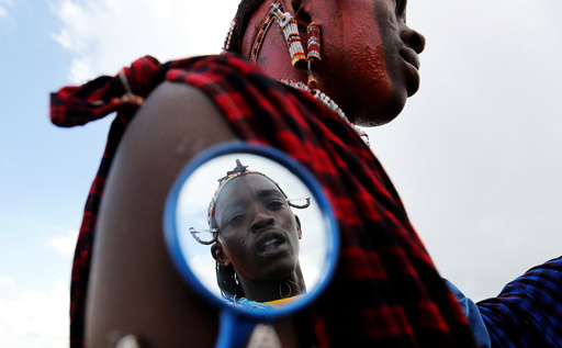 A Maasai moran athlete is reflected in a grooming mirror as he smears his colleague's face with red ocher paint during preparations for the 2016 Maasai Olympics at the Sidai Oleng Wildlife Sanctuary, at the base of Mt. Kilimanjaro, in Kimana