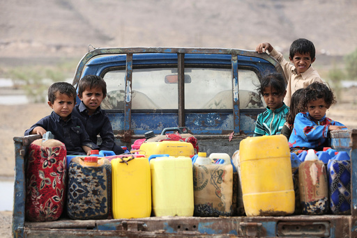 Children ride on the back of a truck loaded with water jerrycans at a camp for internally displaced people in the Dhanah area of the central province of Marib, Yemen