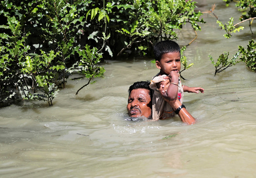 A Rohingya refugee man hols his child as he swims to cross Myanmar-Bangladesh border in Palang Khali