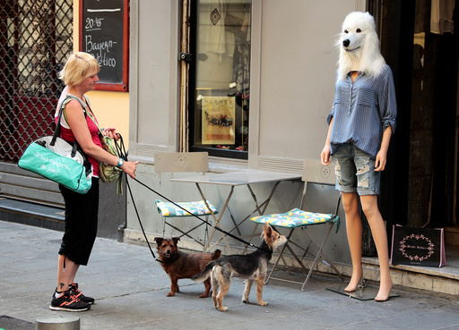 A woman and her dogs stop and look at a store mannequin wearing a dog's head mask outside a fashion shop in Nice
