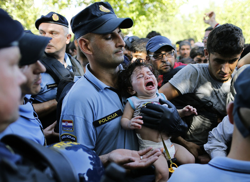 A Croatian policeman holds a crying baby as he stands among migrants waiting to board a bus in Tovarnik