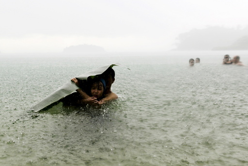 A young girl covers herself from the rain with a banana leaf next to a man in the sea on the outskirts of Colon City