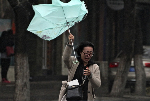 A woman's umbrella is blown by wind during a heavy rain in Yantai