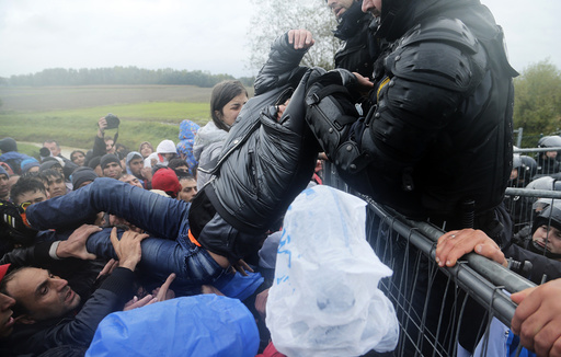 A man is lifted over a fence by Slovenian policemen as migrants attempt to cross the border near Trnovec