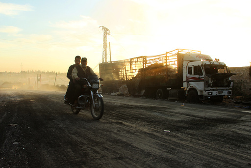 Men drive a motorcycle near a damaged aid truck after an airstrike on the rebel held Urm al-Kubra town