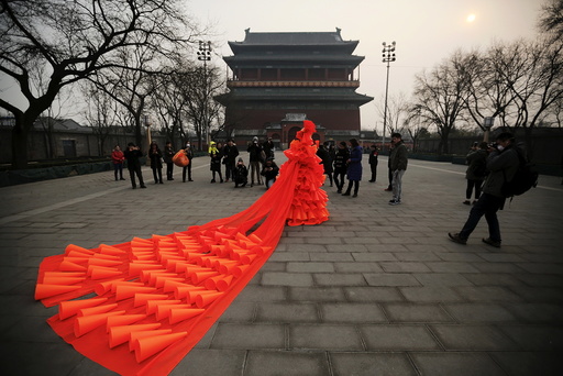 Chinese artist Kong Ning walks in her costume made of hundreds of orange plastic blowing horns during her art performance raising awareness of the hazardous smog in front of the Drum tower in a historical part of Beijing