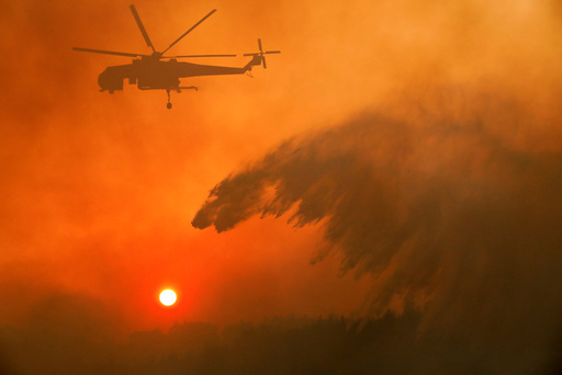 A firefighting helicopter makes water drop as a wildfire burns near the village of Metochi