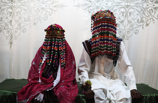 A bride and groom wearing traditional garlands wait for their wedding to start during a mass marriage ceremony in Karachi