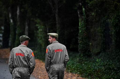 Two visitors dressed in 'Shell' emblazoned mechanics uniforms walk at the annual Goodwood Revival historic motor racing festival, celebrating a mid-twentieth century heyday of the racing circuit, near Chichester in south England