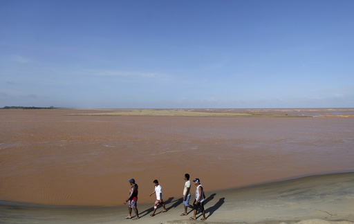 Men walk on the banks of the mouth of Rio Doce, which was flooded with mud after a dam owned by Vale SA and BHP Billiton Ltd burst, as the river joins the sea on the coast of Espirito Santo, in Regencia Village, Brazil