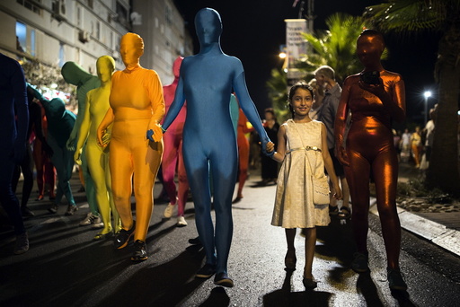 A group of people wearing full solid-coloured bodysuits walk along a promenade as they take part in a street art performance in Bat Yam, near Tel Aviv, Israel