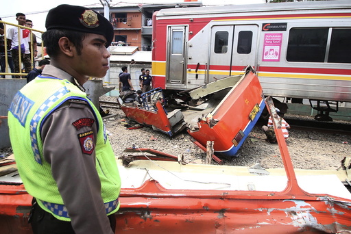 A police officer stands near the scene of an accident between a minibus and a commuter train at a railway crossing in West Jakarta