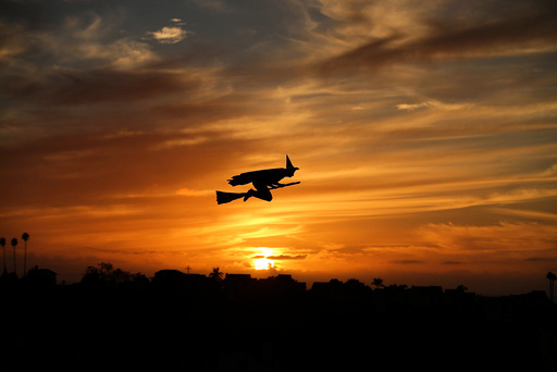 A remote-controlled plane in the form of a witch flies over a neighborhood as the sun sets during Halloween in Encinitas