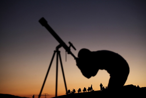 A man observes the sky through a telescope while attending with others an open-air astronomy class in the Samalayuca Desert