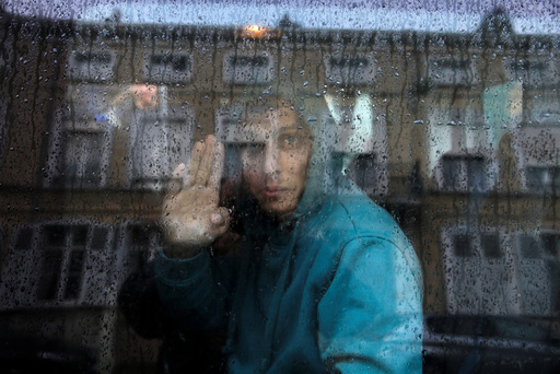 An Afghan adolescent migrant waves from a van as he departs with six others from the emergency shelter for minors in Saint Omer