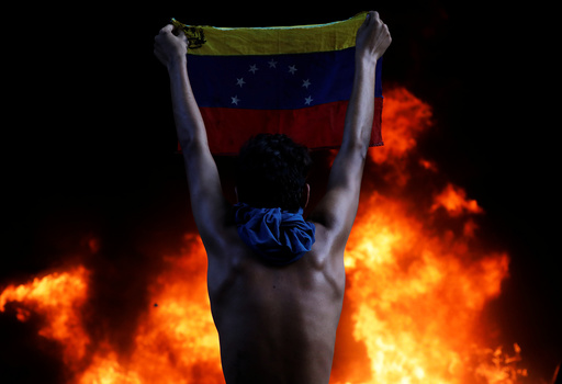 A protester holds a national flag as a bank branch, housed in the magistracy of the Supreme Court of Justice, burns during a rally against Venezuela's President Nicolas Maduro, in Caracas