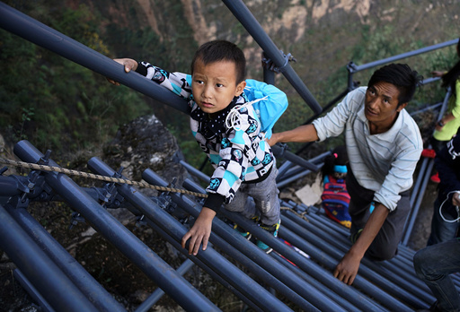 A student from the cliff village in Atule'er climbs newly-constructed steel ladders after school to go home for holidays, in Liangshan