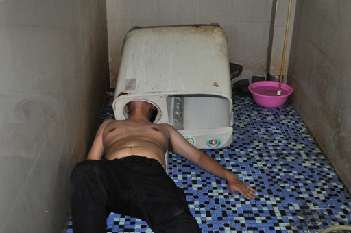 A man lies on the ground as his head is stuck in a washing machine in Fuqing county of Fuzhou