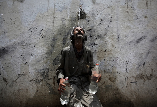 A man cools off from a public tap after filling bottles during intense hot weather in Karachi,