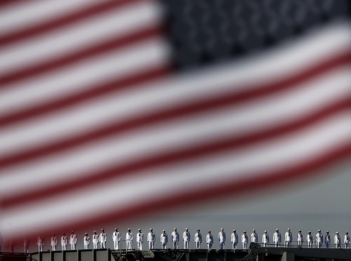The crew members of the USS Ronald Reagan, a Nimitz-class nuclear-powered super carrier, saluting is seen behind the national flag of the U.S. as it arrives at the U.S. naval base in Yokosuka