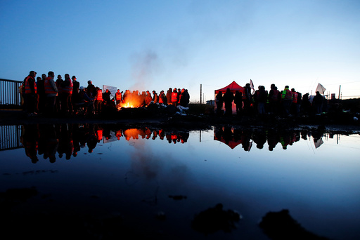 French workers and protestors stand near a burning barricade to block the entrance of the depot of the society SFDM near the oil refinery of Donges