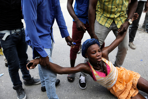 Men help a woman affected by tear gas used by National Police officers to disperse a demonstration of supporters of Fanmi Lavalas political party in the streets of Port-au-Prince, Haiti