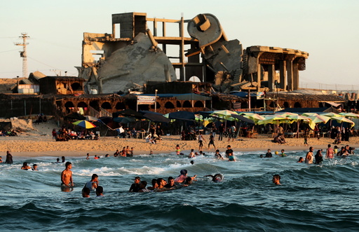A building, that was destroyed in past Israeli shelling, is seen in the background as Palestinians swim in the Mediterranean Sea in the northern Gaza Strip