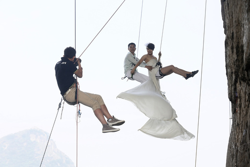 A photographer takes pictures of Fang in a wedding gown next to her husband as they hang from a cliff during a rock climbing exercise in Liuzhou