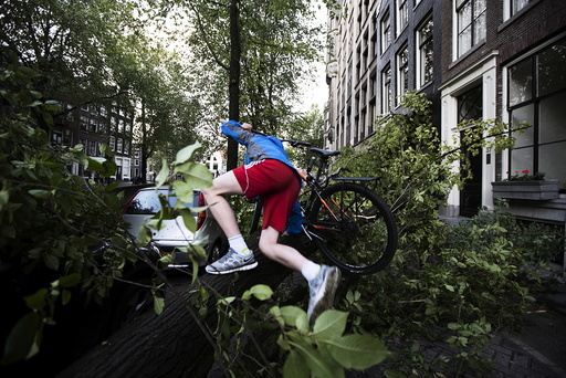 A cyclist climbs over a tree fallen atop a car after a heavy storm in Amsterdam, the Netherlands