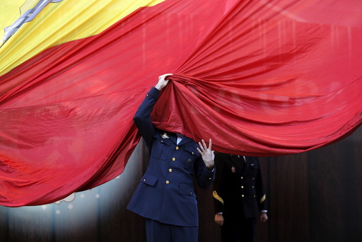 A member of the Spanish Armed Forces gets his face covered by a giant Spanish flag as he helps raise it during a ceremony to mark the 37th anniversary of the 1978 Spanish constitution in Madrid