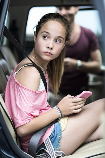 Girl with mobile phone looking away while sitting in car with father in background