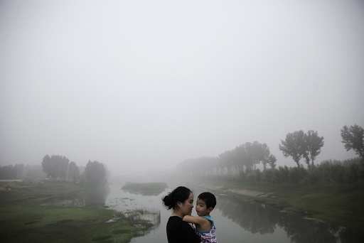 A woman holds a child as travellers wait for the highway from Beijing to China's Hebei Province to reopen after in was closed due to low visibility, on a heavy polluted morning