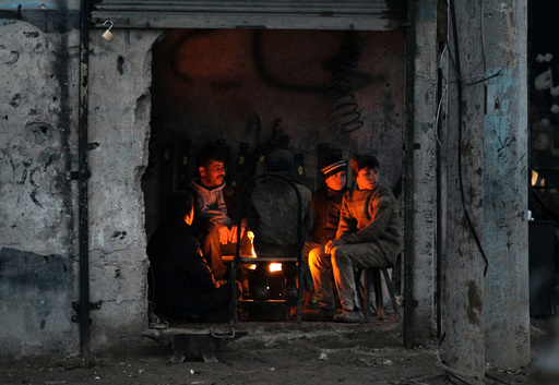 People warm themselves around a fire inside a shop in the Syrian rebel-held town of al-Rai