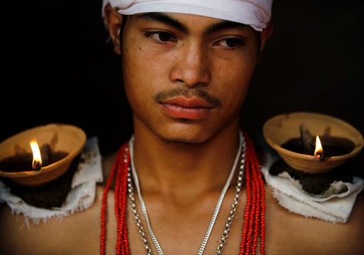 A devotee sits with lit oil lamps on his shoulders while offering prayers during 