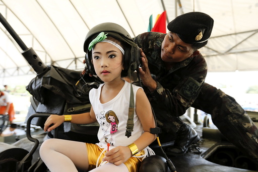 Girl has her helmet adjusted on the top of a tank during the Children's Day celebration at a military facility in Bangkok