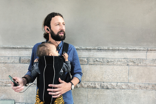 Mid adult father listening music while carrying baby in carrier against wall