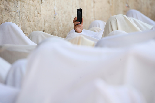 A Jewish worshipper uses his mobile phone to record worshippers who are covered in prayer shawls as they recite the priestly blessing at the Western Wall in Jerusalem's Old City during the Jewish holiday of Sukkot