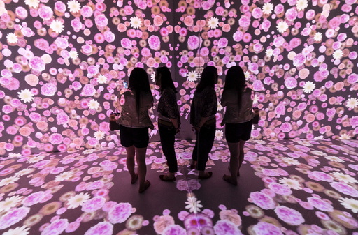 Women are reflected in a mirror as they look at flowers being projected onto the wall and the floor of a room at a shopping mall in Shanghai