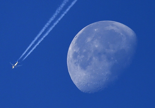 A passenger plane is seen with the moon behind over west London, Britain