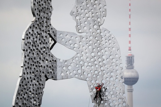 Climbing experts remove a bicycle from Molecule Man sculpture in Berlin