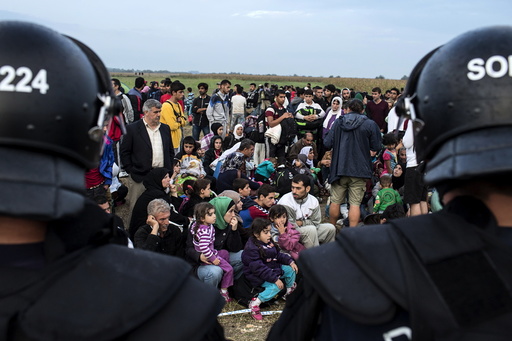 Migrants from Syria sit in front of riot police on a field after crossing into Hungary from the border with Serbia near the village of Roszke
