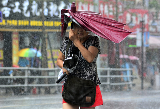 A woman holds her broken umbrella as she walks against strong wind and heavy rainfall as Typhoon Matmo hit Qingdao
