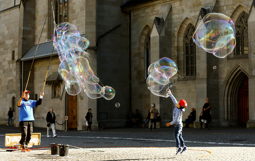 Man blows big soap bubbles during sunny autumn weather at the Muensterhof court in Zurich
